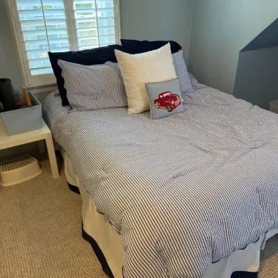 Twin-size bed dressed in blue and white seersucker striped bedding with decorative throw pillows, accompanied by a white bed skirt with...