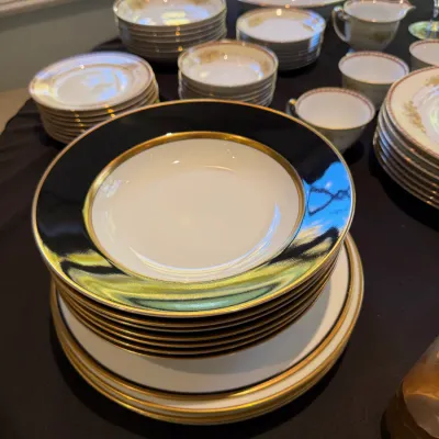 Sale Photo Thumbnail #188: Formal porcelain dinnerware service featuring gold trim and dark cobalt rims, including soup bowls, plates, and teacups.