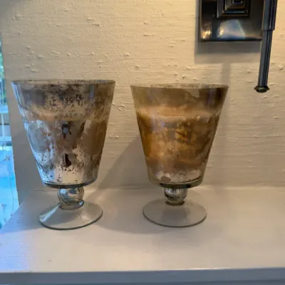 Sale Photo Thumbnail #140: Pair of distressed mercury glass goblet-style candle holders, featuring aged silver and warm gold tones on footed bases.