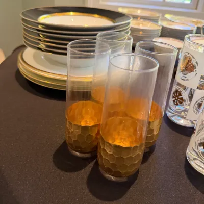 Sale Photo Thumbnail #187: Set of vintage highball glasses with textured honeycomb gold bases, displayed alongside stacks of gold-rimmed china dinnerware.