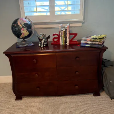Dark wood six-drawer dresser with curved sides, displayed with a desktop globe, bookends, and assorted decor.