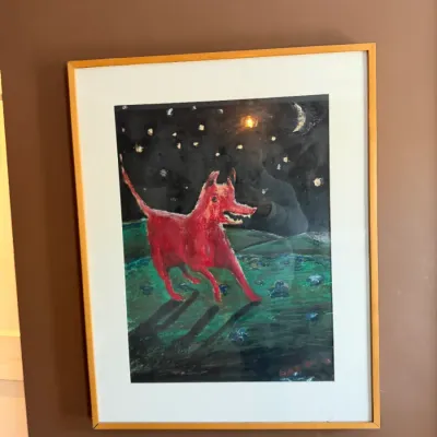 Framed folk art style painting depicting a red dog under a starry night sky, set in a slim wooden frame with a white mat.