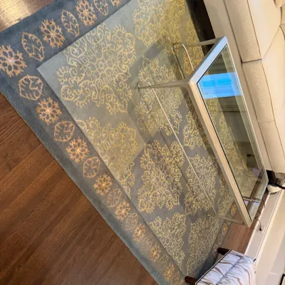 Sale Photo Thumbnail #109: Large muted teal and gold patterned area rug positioned beneath a glass-top coffee table on hardwood flooring.