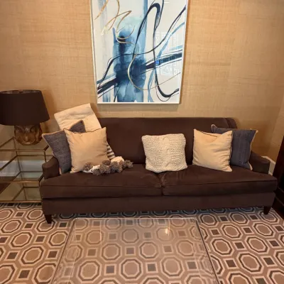 Brown velvet upholstered sofa lined with throw pillows, centered below a large framed abstract art piece in blue and gold tones.