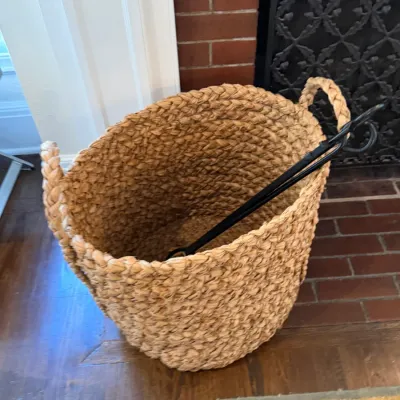 Sale Photo Thumbnail #141: Large woven seagrass basket with braided handles containing a pair of black wrought iron fireplace tongs.