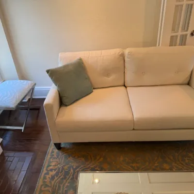 Sale Photo Thumbnail #137: Contemporary cream fabric loveseat featuring subtle button tufting on the back cushions, paired with a green accent pillow, a pattern area rug, and an X-frame vanity stool.