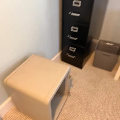 Beige metal personal safe sitting beside a tall black filing cabinet in an office space.