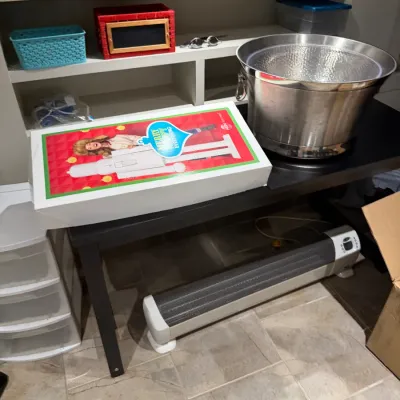 Sale Photo Thumbnail #265: Large stainless steel hammered beverage tub sitting on a black table alongside a boxed HSN holiday nutcracker decoration, with an electric baseboard space heater beneath.