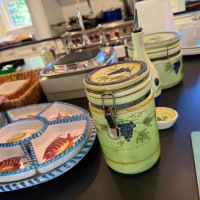Sale Photo Thumbnail #200: Hand-painted Italian style ceramic kitchenware, including a grape-motif canister set and a segmented fish-motif serving platter displayed on a counter.