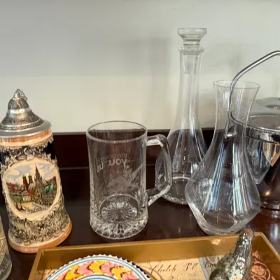 Sale Photo Thumbnail #164: Collection of barware and glassware, including a ceramic German beer stein with pewter lid, clear glass decanters, a glass mug, and a chrome ice bucket.