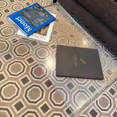 Sale Photo Thumbnail #208: Modern clear acrylic waterfall coffee table displaying several art and design hardcover books, resting on a geometric patterned rug.