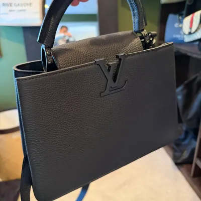 Black Louis Vuitton Capucines BB handbag in pebbled Taurillon leather, featuring matte black LV hardware, top handle, and shoulder strap.