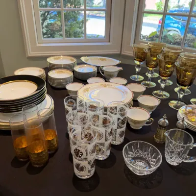 Sale Photo Thumbnail #185: Collection of vintage tableware including amber stemware, black and gold trim porcelain plates, mid-century printed glasses, and cut crystal serving pieces.