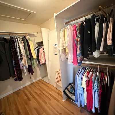 Walk-in closet filled with various men's and women's clothing items, including coats, jackets, shirts, and tops, hung on...