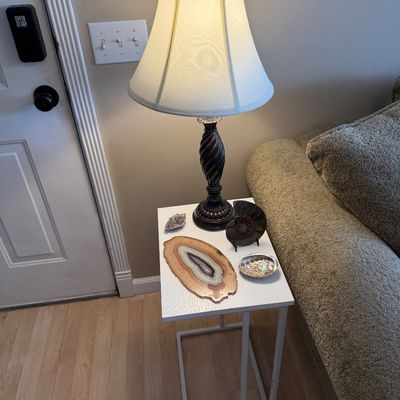 Traditional table lamp with a dark twisted post base and fabric bell shade, sitting on a modern white C-shaped side table displayed...