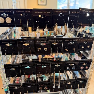 Rotating clear acrylic jewelry display rack filled with various styles of sterling silver earrings on black retail cards.