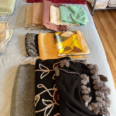 Collection of assorted women's scarves, shawls, and wraps in various fabrics, colors, and patterns laid out on a bed.