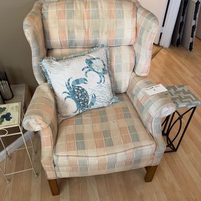 Plaid upholstered wingback chair with wooden legs, accessorized with a fringe-trimmed coastal crab throw pillow.