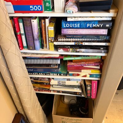 Shelves filled with a variety of books, office supplies, and household items alongside a U-Haul cardboard box.
