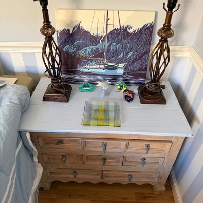 Rustic wooden dresser topped with a pair of open-cage bronze table lamps, a sailboat canvas art print, and small decorative trinkets.