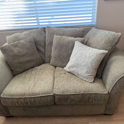 Contemporary oversized plush loveseat with rolled arms, textured sage green upholstery, and matching throw pillows.
