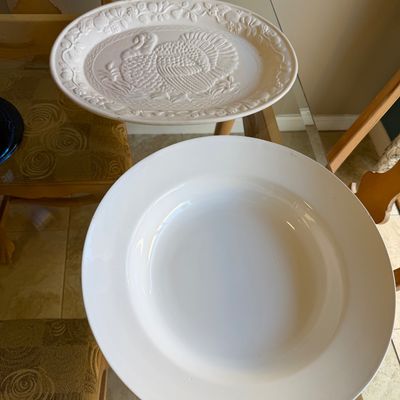 Two white ceramic platters, including one featuring a embossed turkey and fruit motif along the rim.