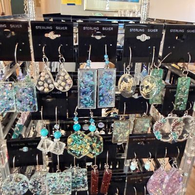 A retail jewelry display filled with assortment of resin, bead, and crushed glass dangling earrings, all mounted on black sterling silver...