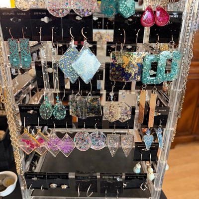 Rotating clear acrylic jewelry display rack filled with handmade resin, glitter, pressed flower, and stone dangle earrings on sterling...
