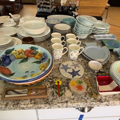 Large assortment of ceramic dinnerware, mugs, coastal-themed serveware, and decorative kitchen accessories arranged on a granite countertop.