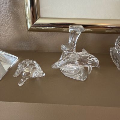 Collection of clear crystal animal figurines, including a small sea turtle and a dolphin leaping over a wave, displayed on a shelf.