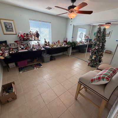 Spacious room featuring tables displayed with holiday decor, plush snowmen, a pre-lit Christmas tree, and upholstered accent chairs with...