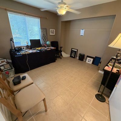 Home office and display area featuring dining chairs, a desk draped in black cloth with various electronics, artwork, and a standing...