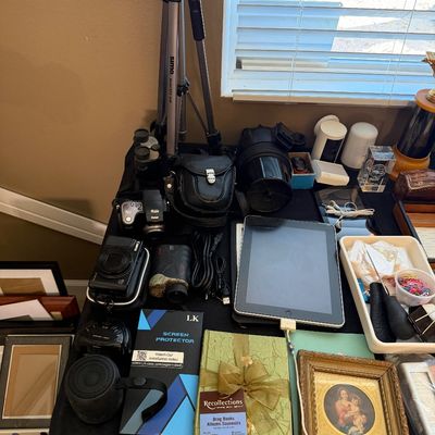 Collection of electronics and household items including an iPad, digital and film cameras, a camera tripod, small speakers, and framed...