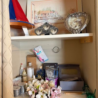 Shelves filled with various items including a model sailboat, framed art prints, decorative heart-shaped photo frames, faux flowers, and...