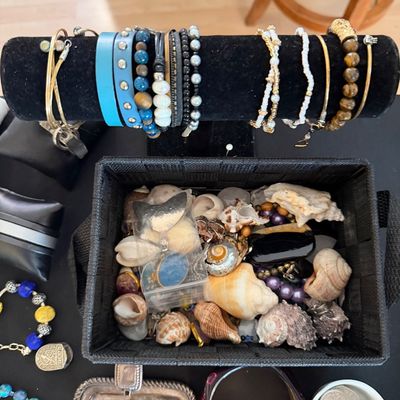 Collection of fashion jewelry displayed on a T-bar stand alongside a woven bin filled with seashells, loose beads, and small accessories.