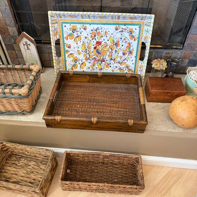 Collection of decorative serving trays and woven storage baskets, including a colorful hand-painted rooster tray and a rustic dark wood...