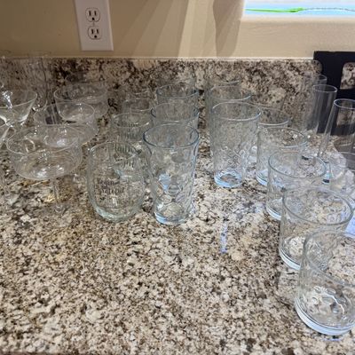 Large assortment of clear glassware arranged on a granite countertop, including bubble-texture tumblers, stemless wine glasses with...