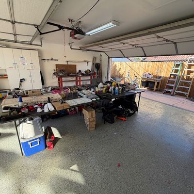 Garage sale setup featuring folding tables displaying various hand tools, hardware, household supplies, and a blue cooler.