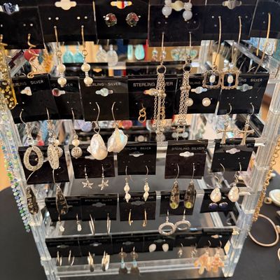 A rotating clear acrylic jewelry display rack filled with various styles of sterling silver earrings on black cards, including pearls,...
