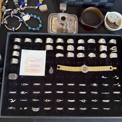 Jewelry tray filled with sterling silver bands and silver plate spoon rings, displayed alongside beaded bracelets, a gold-tone watch, and...