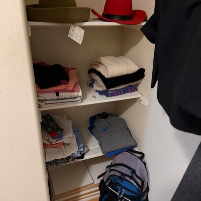 Closet shelves filled with folded clothing, brimmed hats, and a grey and blue backpack.