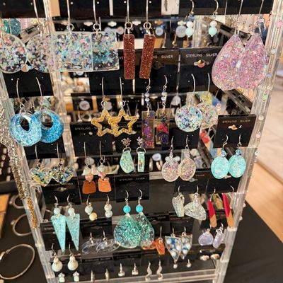Rotating clear acrylic display stand filled with assorted handcrafted resin and glitter dangle earrings on sterling silver jewelry cards.