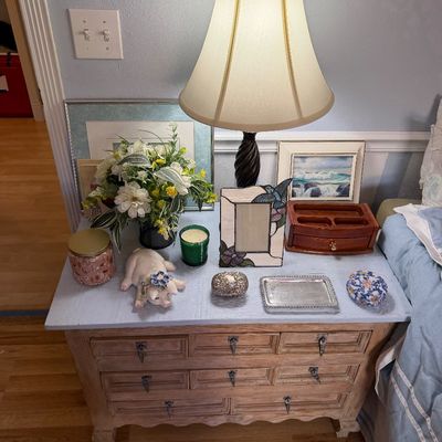 A vintage table lamp with a twisted base and cream shade set atop a light wood multi-drawer nightstand, surrounded by decorative tabletop...
