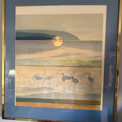 Framed coastal art print depicting shorebirds along a beach, housed under glass in a polished gold-tone metal frame with blue matting.