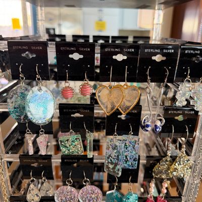 Rotating display stand showcasing various pairs of sterling silver dangle and drop earrings, featuring glitter resin, pressed flowers,...