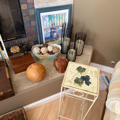 Collection of home decor items featuring a wrought iron plant stand with a painted grape tile top, framed wall art, decorative candles in...