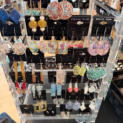 A acrylic display stand filled with various handcrafted drop and dangle earrings, featuring resin, dried flower, and glitter designs.