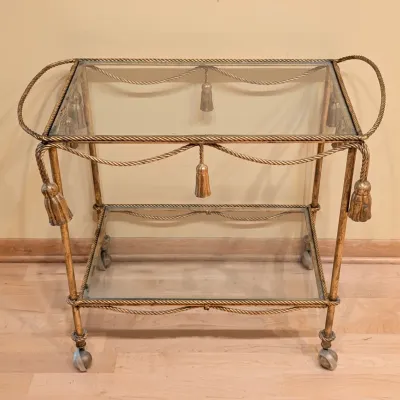 Sale Photo Thumbnail #4: Vintage Hollywood Regency Gold-Gilt Rope & Tassel Design Bar Cart. Hollywood Regency-style gold-gilt bar cart or serving cart with an ornate rope-and-tassel frame, mirrored glass shelves, and caster wheels. The decorative tassel and twisted-rope details g