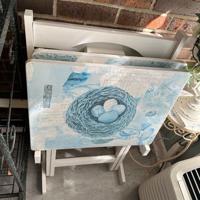 Sale Photo Thumbnail #8: Set of white wooden folding TV dinner tray tables with a storage rack, featuring blue collage-style bird and nest graphic tops.