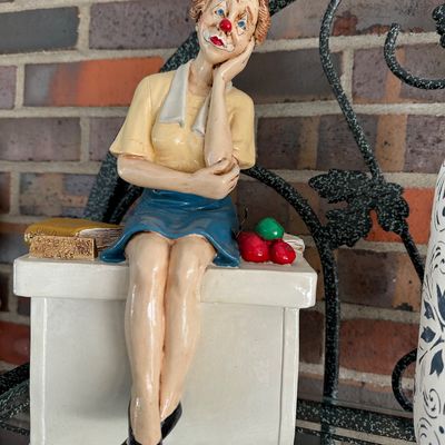 Sale Photo Thumbnail #6: Vintage painted ceramic figurine depicting a female schoolteacher clown seated at a desk, featuring detailed hand-painted elements.